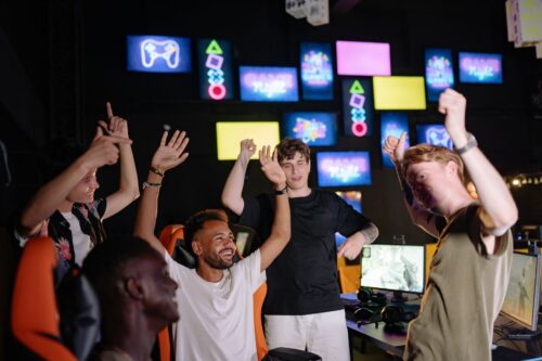 Joueurs en salle gaming qui lèvent les bras après une victoire, illustrant l’esprit d’équipe.
